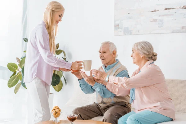 Junge Frau schenkt Senioren Tassen mit Tee — Stockfoto