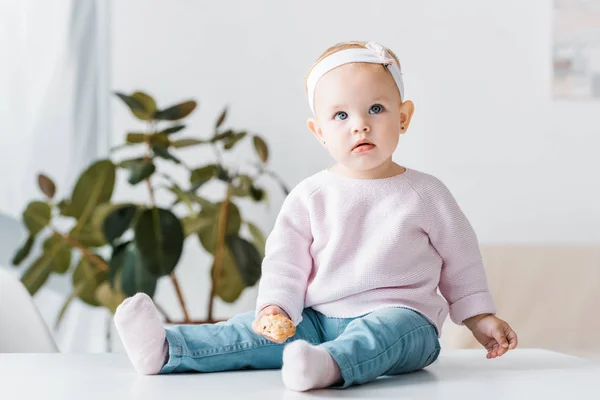 Cute baby sitting on white table and holding biscuit — Stock Photo