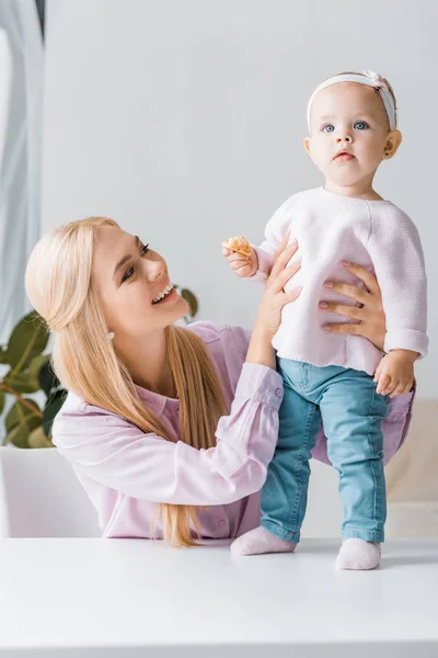 Young mother looking at small cute daughter with cookie — Stock Photo