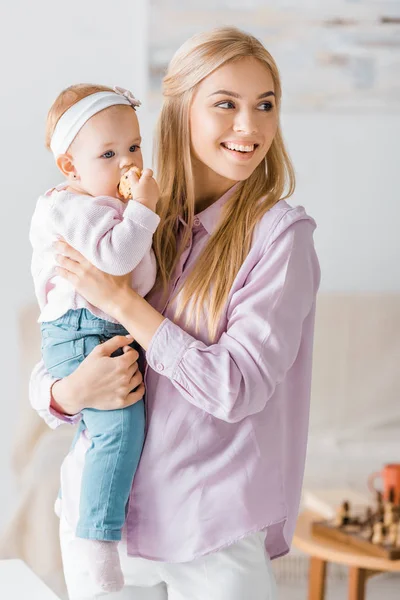 Молодая мама держит маленькую симпатичную дочь с печеньем — стоковое фото