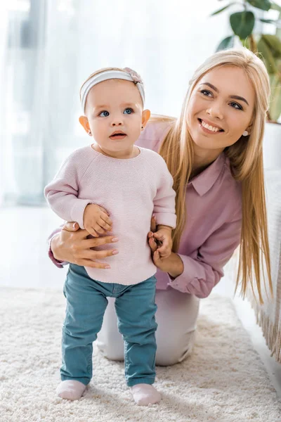 Young mother sitting on carpet and holding cute toddler daughter — Stock Photo
