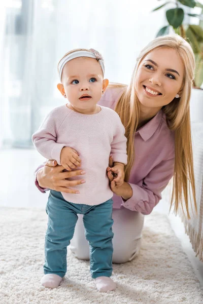 Jeune mère assis sur le tapis et tenant mignon tout-petit fille — Photo de stock