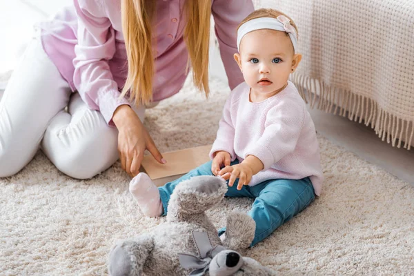 Mutter sitzt mit kleiner Tochter auf Teppich und spielt mit Spielzeug — Stockfoto