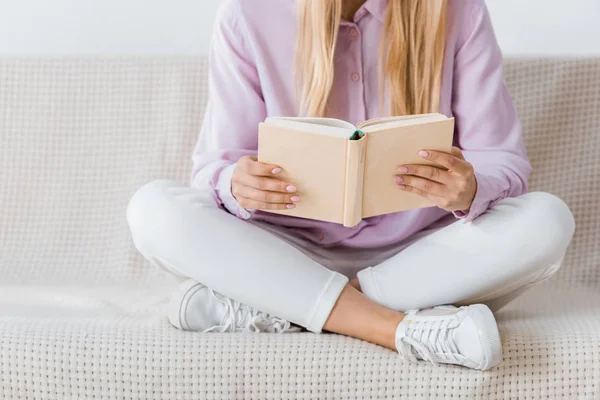 Mulher lendo livro e sentado no sofá com pernas cruzadas — Fotografia de Stock