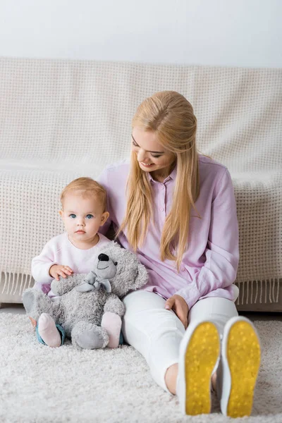 Junge Frau sitzt mit Tochter und Teddybär auf dem Boden — Stockfoto