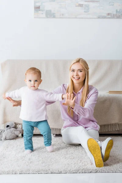 Young woman sitting on floor and holding daughter — Stock Photo