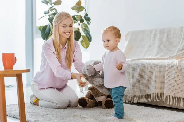 Young woman with little daughter playing toys on carpet — Stock Photo