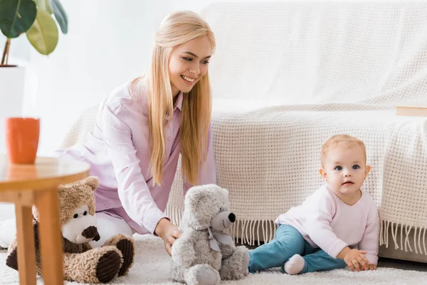 Mujer joven con linda hija jugando juguetes en la alfombra — Stock Photo