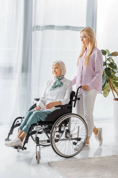 Young woman pushing wheelchair with senior woman in nursing home — Stock Photo