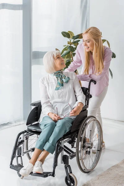 Mujer joven hablando con una mujer mayor en silla de ruedas en un hogar de ancianos - foto de stock
