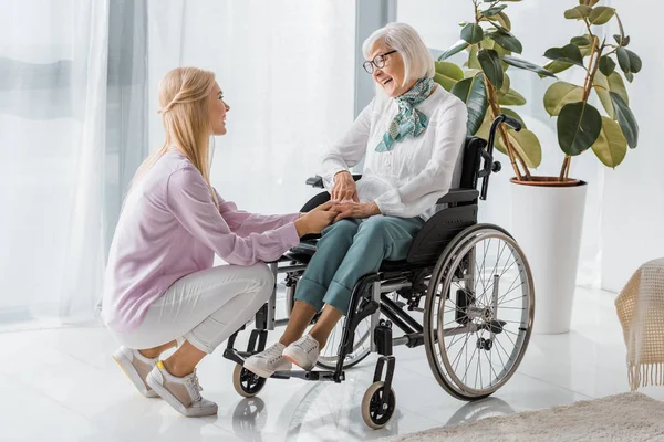Mujer joven hablando con una mujer mayor en silla de ruedas en un hogar de ancianos - foto de stock