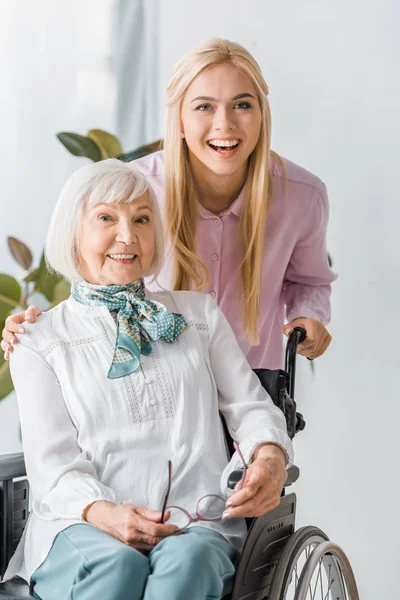 Mulheres jovens e idosas em cadeira de rodas sorrindo e olhando para a câmera — Fotografia de Stock