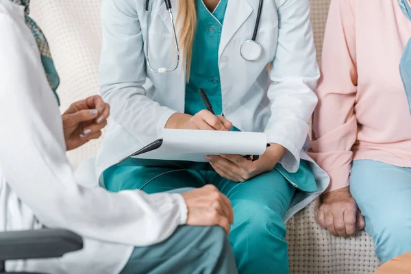 Close up of female young doctor writing prescription to senior women — Stock Photo