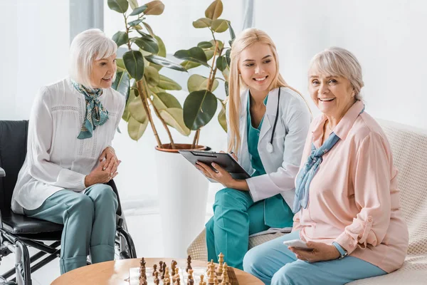 Giovane infermiera seduta sul divano e che scrive prescrizione alle donne anziane — Foto stock