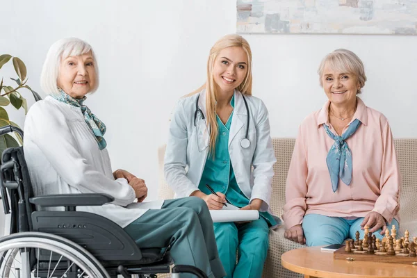 Junge Krankenschwester sitzt auf Sofa und schreibt Rezepte an ältere Frauen — Stockfoto