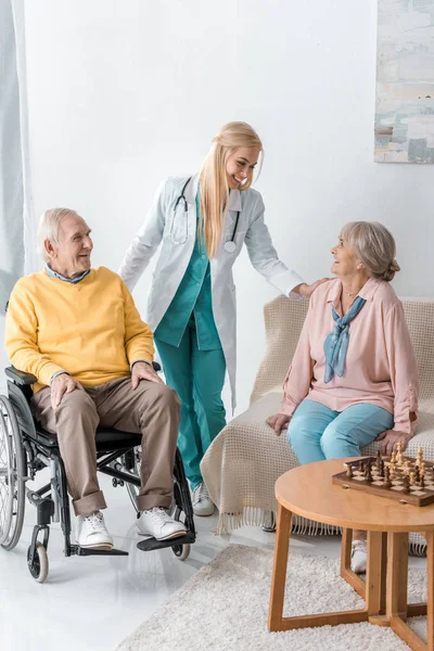 Giovane medico femminile allegro che parla con gli anziani a casa di cura — Foto stock