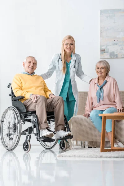 Jovem médico feminino alegre conversando com pessoas idosas em casa de repouso — Fotografia de Stock