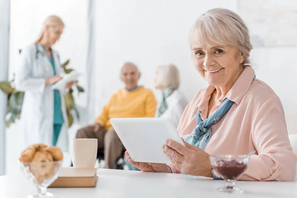 Пожилая женщина с помощью цифрового планшета за столом в доме престарелых — стоковое фото