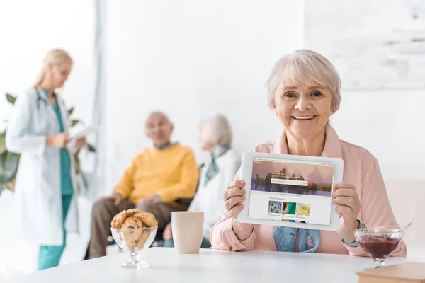 Senior woman showing shutterstock app on digital tablet screen at nursing home — Stock Photo