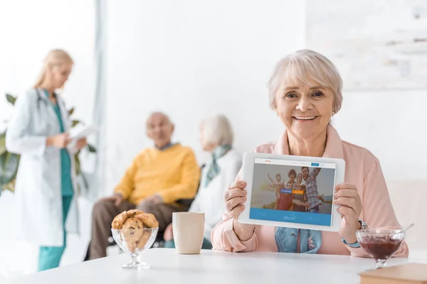 Senior woman showing couchsurfing app on digital tablet screen at nursing home — Stock Photo