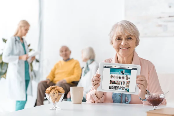 Пожилая женщина показывает приложение Amazon на экране цифрового планшета в доме престарелых — стоковое фото