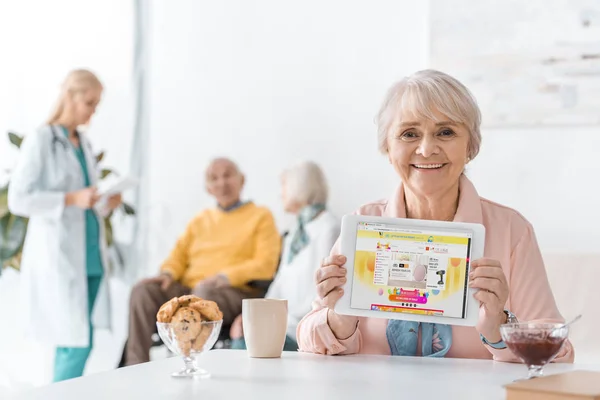 Seniorin zeigt aliexpress-App auf digitalem Tablet-Bildschirm im Pflegeheim — Stock Photo