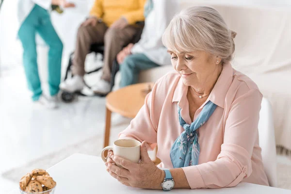 Пожилая женщина держит и смотрит на чашку — стоковое фото