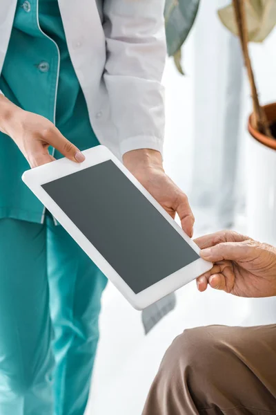 Primer plano en el médico y las manos de pacientes mayores sosteniendo tableta digital con pantalla en blanco - foto de stock