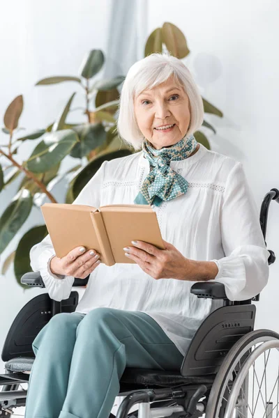 Счастливая пожилая женщина, сидящая в инвалидной коляске и читающая книгу — стоковое фото