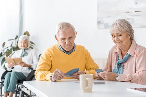 Pacientes mayores jugando a las cartas en la mesa en la clínica - foto de stock