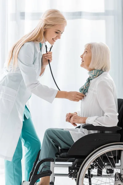 Joven médico examinando con estetoscopio discapacitado mujer mayor - foto de stock