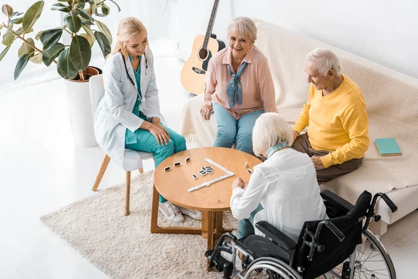 Jeune infirmière jouant domino avec des patients âgés dans une maison de soins infirmiers — Photo de stock