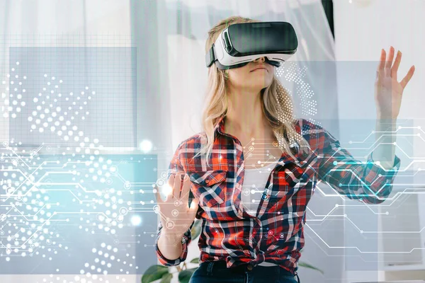 Mujer joven con auriculares de realidad virtual apuntando a las señales de seguridad cibernética en la habitación - foto de stock