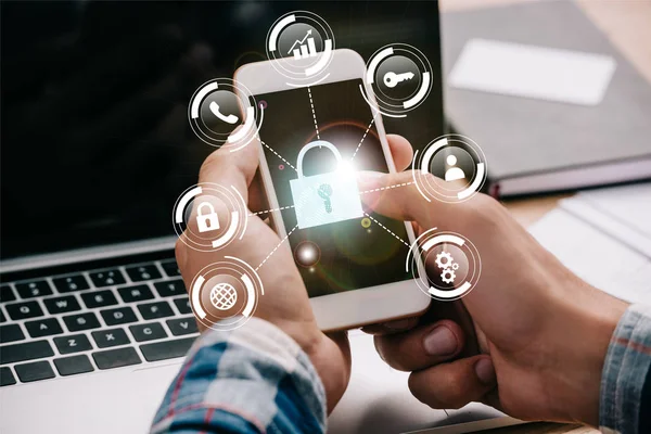 Cropped shot of businessman using smartphone with cyber security signs at workplace with laptop — Stock Photo