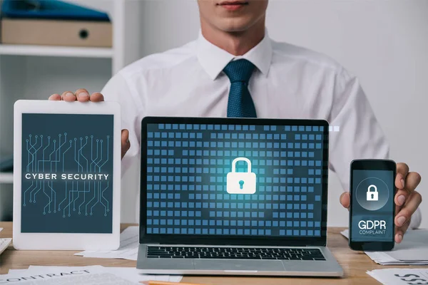 Cropped shot of businessman showing laptop, tablet and smartphone with gdpr and cyber security signs on screens at workplace in office — Stock Photo