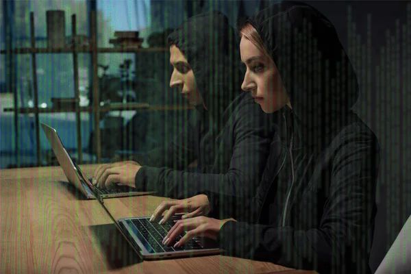 Side view of hackers in black hoodies using laptops at wooden tabletop, cyber security concept — Stock Photo