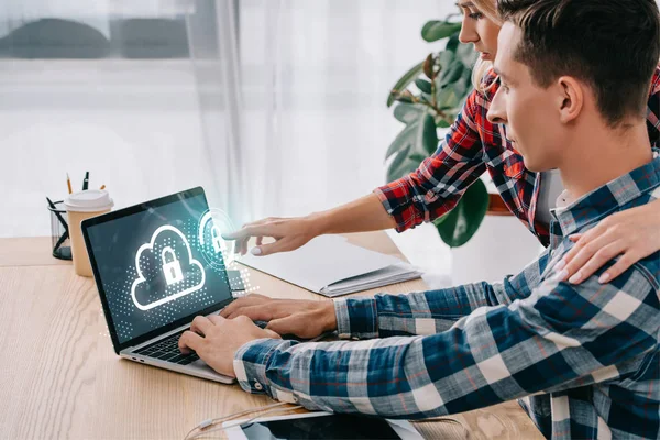 Businesswoman pointing at laptop with cloud and lock sign on screen while taking part in webinar together with colleague in office — Stock Photo