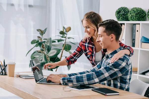 Empresaria apuntando a la pantalla del ordenador portátil en blanco mientras participa en webinar junto con su colega en la oficina - foto de stock
