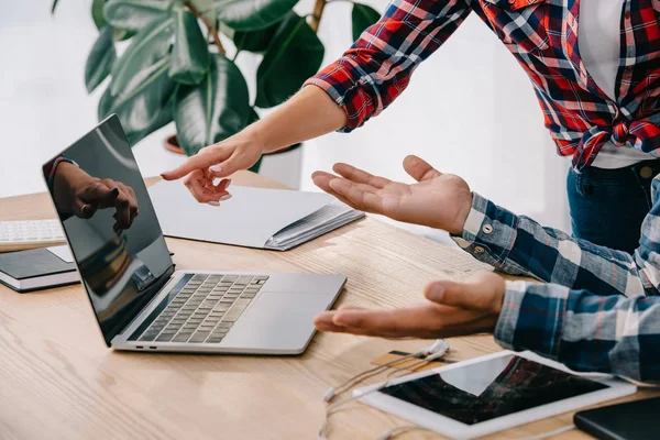 Visión parcial de la mujer de negocios apuntando a la pantalla del ordenador portátil en blanco mientras participa en el seminario web junto con su colega en la oficina - foto de stock