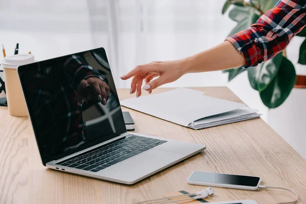 Visão parcial da mulher apontando para laptop com tela em branco na mesa com smartphone e café para ir — Fotografia de Stock