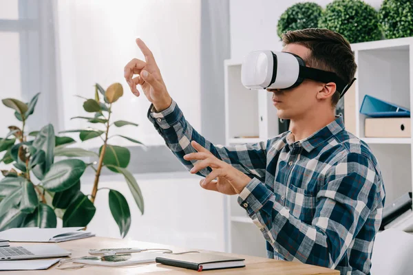 Hombre de negocios con auriculares de realidad virtual gesticulando en el lugar de trabajo con portátil en la oficina - foto de stock