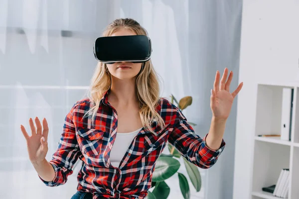Mujer joven con auriculares de realidad virtual haciendo gestos en la habitación - foto de stock