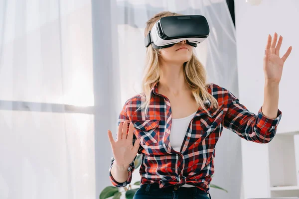 Mujer joven con auriculares de realidad virtual haciendo gestos en la habitación - foto de stock