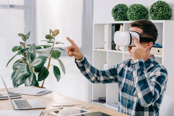 Vista laterale dell'uomo d'affari in realtà virtuale auricolare gesticolare sul posto di lavoro con laptop in ufficio — Foto stock