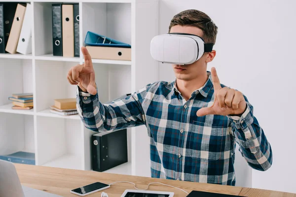 Portrait of man in virtual reality headset at tabletop with smartphone, tablet and laptop — Stock Photo