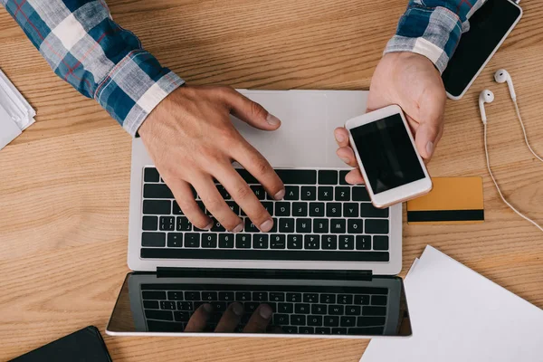 Partial view of man using smartphone and laptop at tabletop with credit card — Stock Photo