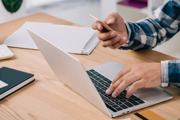 Partial view of man using smartphone and laptop at tabletop with credit card — Stock Photo