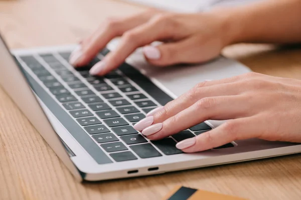 Teilansicht einer Frau, die mit Kreditkarte auf Laptop am Tisch tippt — Stockfoto