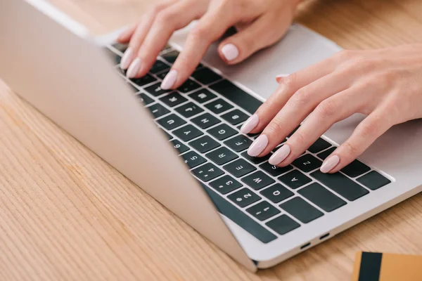 Partial view of woman typing on laptop at tabletop with credit card — Stock Photo