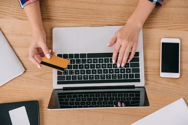 Partial view of woman with credit card making purchase online at wooden tabletop — Stock Photo